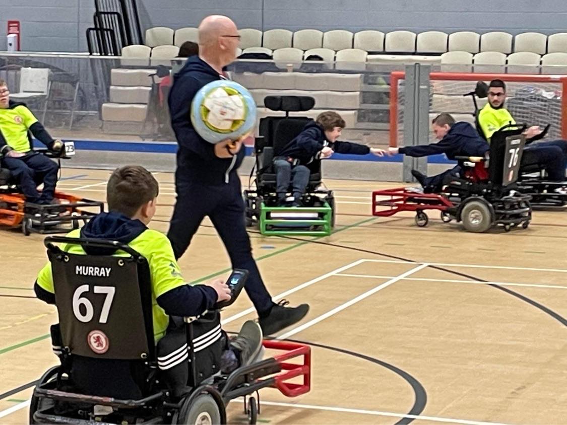 A powerchair football game in progress. Two players celebrate with a fist pump