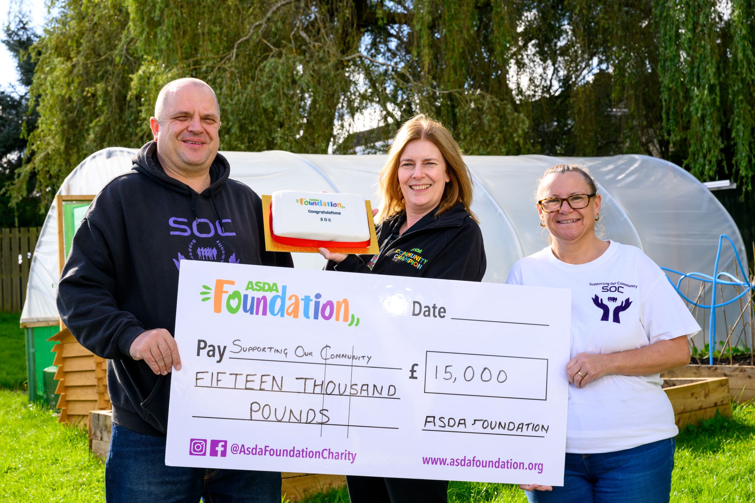 Three people holding a large Asda Foundation cheque and cake.